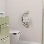 PLUS Toilet Paper holder and grab bar installed close to a white toilet and a green vanity.